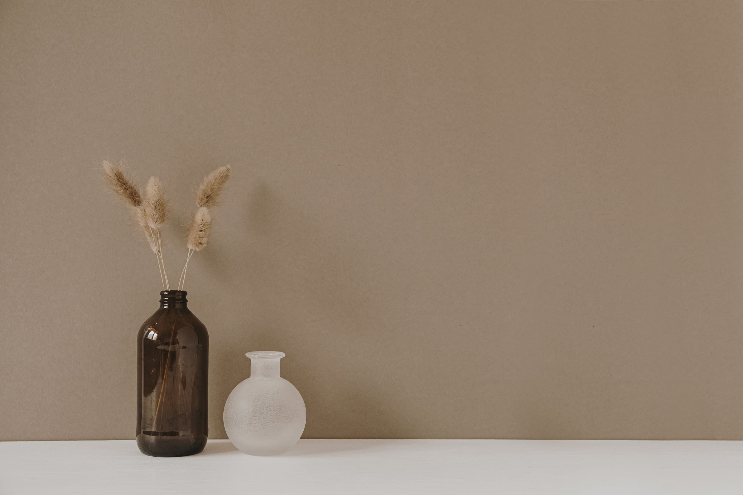 Glass Bottle Vases on White Table and Brown Wall Background